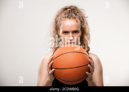 Young female basketball player holding ball by her face while looking at you Stock Photo