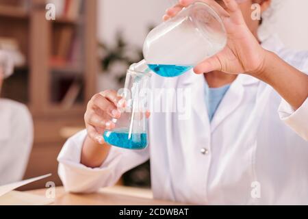 Hands of youthful mixed-race schoolgirl pouring blue fluid from bottle into tube Stock Photo