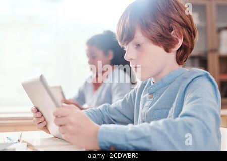 Serious clever schoolboy with touchpad looking through online document Stock Photo