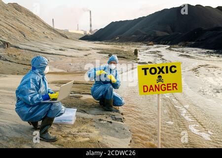 Two ecologists in protective coveralls studying characteristics of toxic water Stock Photo