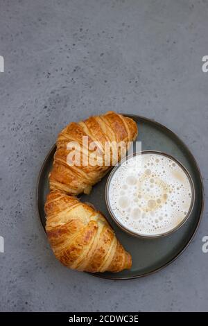 Cup of cappuccino coffee and two fresh croissants on grey stone table. French breakfast. Stock Photo