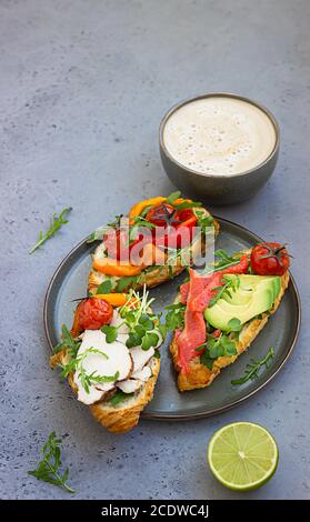 Breakfast or lunch with coffee and different croissant sandwiches with grilled pepper, tomatoes, smoked salmon, turkey, avocado and arugula served wit Stock Photo
