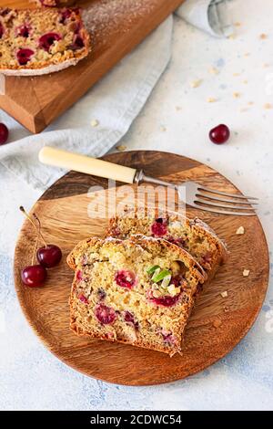 Homemade sweet cherry loaf cake with nuts on wooden plate. Light blue background. Selective focus. Stock Photo