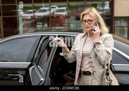 Mature serious busy woman in eyeglasses and grey elegant casualwear Stock Photo