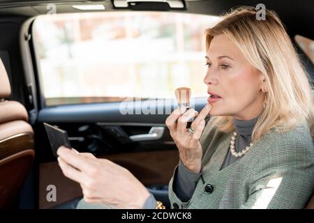 Mature blond businesswoman applying blush or powder on face in taxi cab Stock Photo