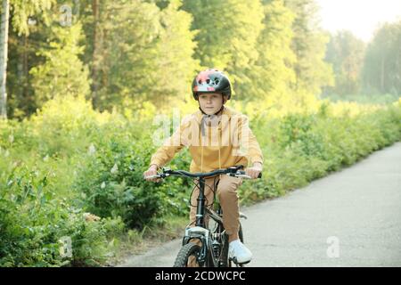 Schoolboy in casualwear and protective helmet riding new bicycle along road Stock Photo