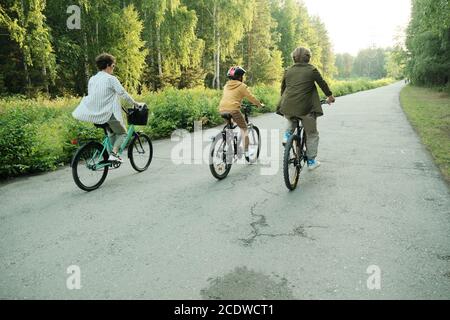 Active family of father, mother and son in casualwear riding bicycles along road Stock Photo
