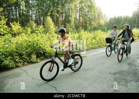 Young couple and their son riding bicycles along road in natural environment Stock Photo