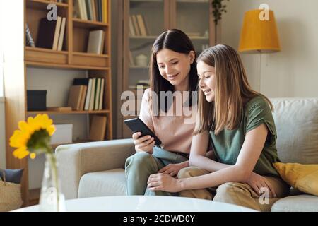 Young smiling female showing photos in the phone to her cute teenage daughter Stock Photo