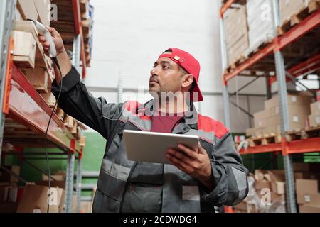 Young serious mixed-race manager of warehouse with touchpad scanning codes Stock Photo