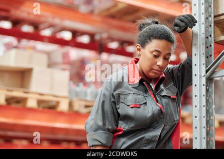 Young tired mixed-race female in uniform and gloves leaning against rack Stock Photo