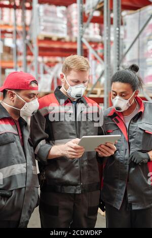 Group of contemporary intercultural warehouse workers in respirators and uniform Stock Photo