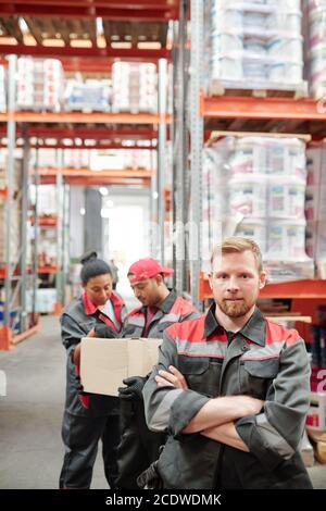 Bearded man in workwear standing in front of camera on background of colleagues Stock Photo