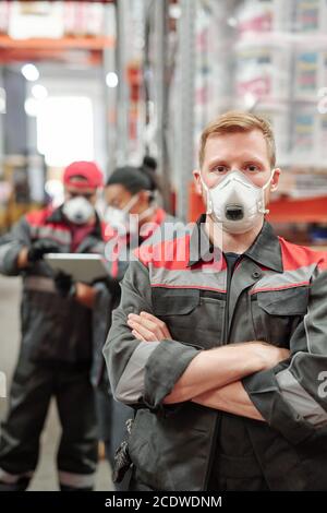 Young blond man in workwear and protective respirator crossing his arms by chest Stock Photo