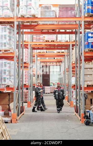 Young mixed-race male warehouse worker in uniform moving along aisle Stock Photo