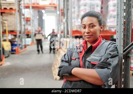Serious young mixed-race woman in workwear and gloves crossing arms by chest Stock Photo