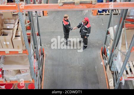 Overview of two young intercultural managers of warehouse hall shaking hands Stock Photo