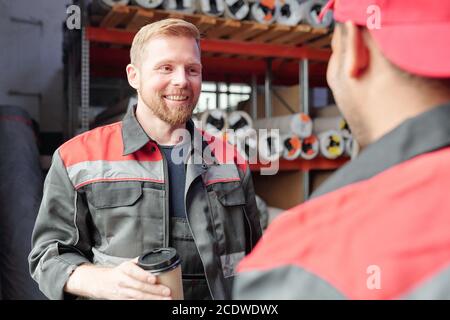 Smiling worker in uniform having coffee during conversation with colleague Stock Photo
