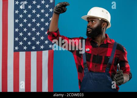 Young builder of African ethnicity in hardhat, gloves, overalls and flannel Stock Photo