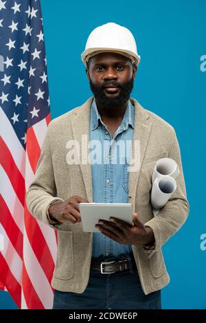 Young bearded African-american engineer using tablet and holding blueprints Stock Photo