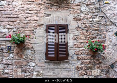 Typical Italian Window With Closed Wooden Shutters, Decorated With Fresh Flowers Stock Photo