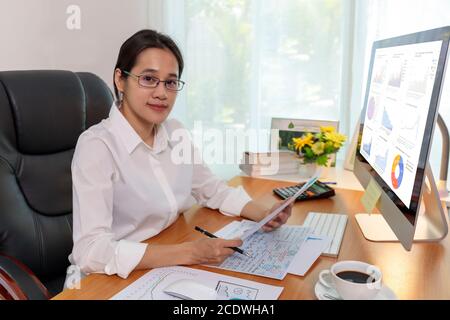 Business women smileing  wear glasses hands holding paper and pencil. business people analysis chart data on computer PC screen at office. Business at Stock Photo