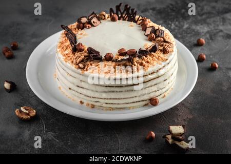 white cream honey cake with walnuts, hazelnuts and sweets on grey cement background, food and homemade baking concept in rustic style Stock Photo