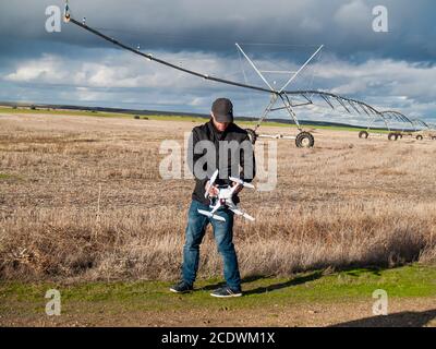 A drone pilot configuring his drone in a field with and irrigation system before flying Stock Photo