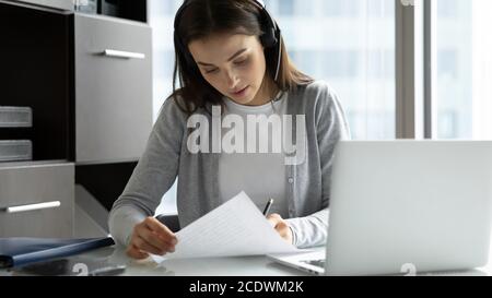 Focused businesswoman wearing headset writing notes, using laptop Stock Photo