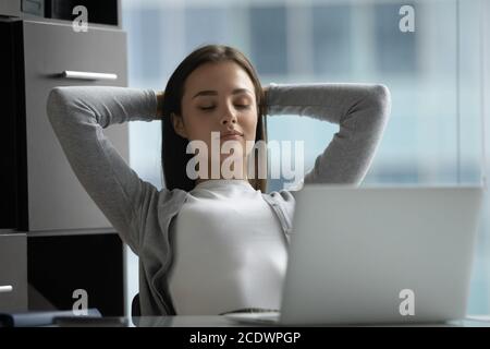 Peaceful satisfied young businesswoman stretching hands, relaxing in office Stock Photo