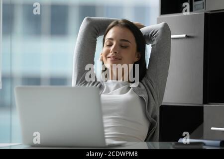 Smiling peaceful young businesswoman leaning back in comfortable office chair Stock Photo