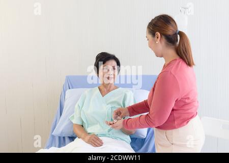 An elderly Asian woman is being taken care of by her relatives in the hospital recovery room. Stock Photo