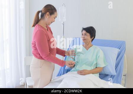 An elderly Asian woman is being taken care of by her relatives in the hospital recovery room. Stock Photo