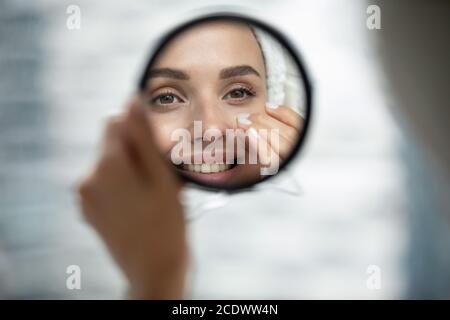 Close up smiling beautiful woman looking in small round mirror Stock Photo