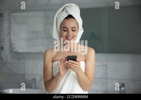 Smiling young woman using smartphone after shower in bathroom Stock Photo