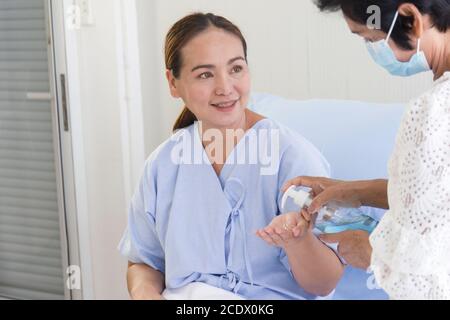 A young Asian woman who was ill in a hospital lay on a recovery bed. Her mother, who was taking care of her side, was using alcohol gel to wash her ha Stock Photo
