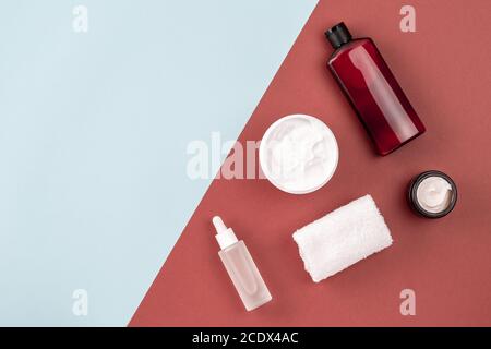 Skin care products on brown and blue surface. Frame from shampoo or cosmetic lotion bottle, towel, open cream jar, serum with peptides. Beauty, spa Stock Photo