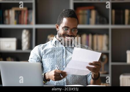 Happy smiling African American man reading letter at workplace Stock Photo