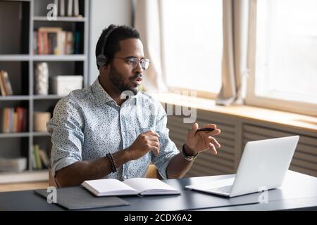 African American man wearing headphones speaking, using laptop Stock Photo