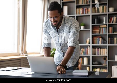 Smiling African American businessman standing near desk, using laptop Stock Photo