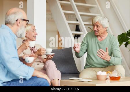 Senior man talking to his friends while they sitting on sofa and drinking tea in the room Stock Photo