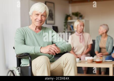 Portrait of senior disabled man smiling at camera with two women drinking tea in the background Stock Photo