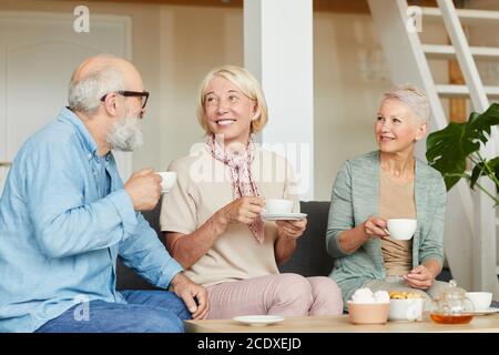 Group of happy senior people smiling to each other and drinking tea at home Stock Photo