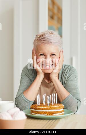 Portrait of happy senior woman sitting at the table with cake with candles and smiling at camera Stock Photo