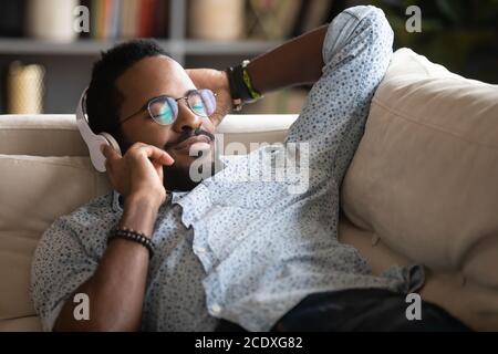 Satisfied relaxed African American man enjoying favorite music on couch Stock Photo