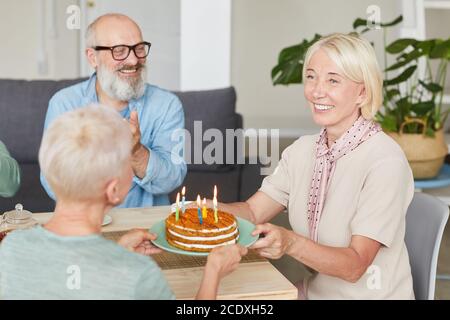 Happy senior friends celebrating birthday with birthday cake of their friend at the table at home Stock Photo