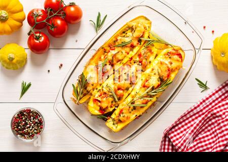 Stewed yellow zucchini with tomatoes and onions, cheese and herbs, carrots and spices, stuffed zucchini on a white wooden background Stock Photo