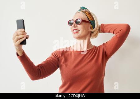 Mature woman in sunglasses making selfie on her mobile phone against the white background Stock Photo