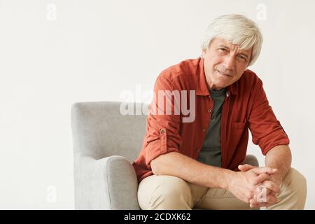 Portrait of mature man in casual clothing sitting on armchair against the white background Stock Photo