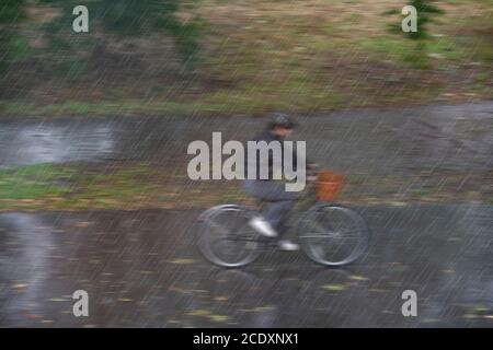 A soaked girl rides through the driving rain on her bike Stock Photo